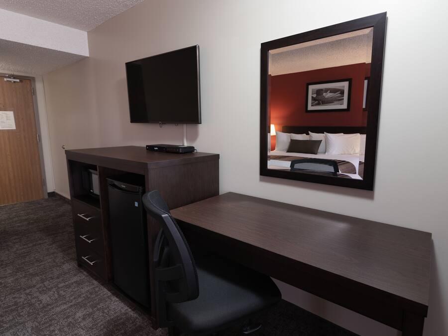 Een hotelkamer met een bureau, stoel, televisie en een bed met hoofdeinde.