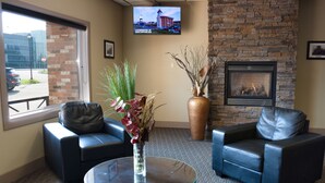 Un hall con dos sillones de cuero, una mesa de centro de vidrio, un jarrón con flores, una chimenea y un televisor en la pared.