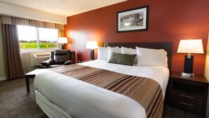 Una habitación de hotel con una cama grande, dos mesitas de noche con lámparas, una silla y una ventana con cortinas.
