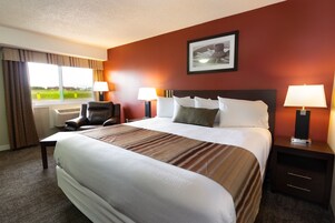 Una habitación de hotel con una cama grande, dos mesitas de noche con lámparas, una silla y una ventana con cortinas.