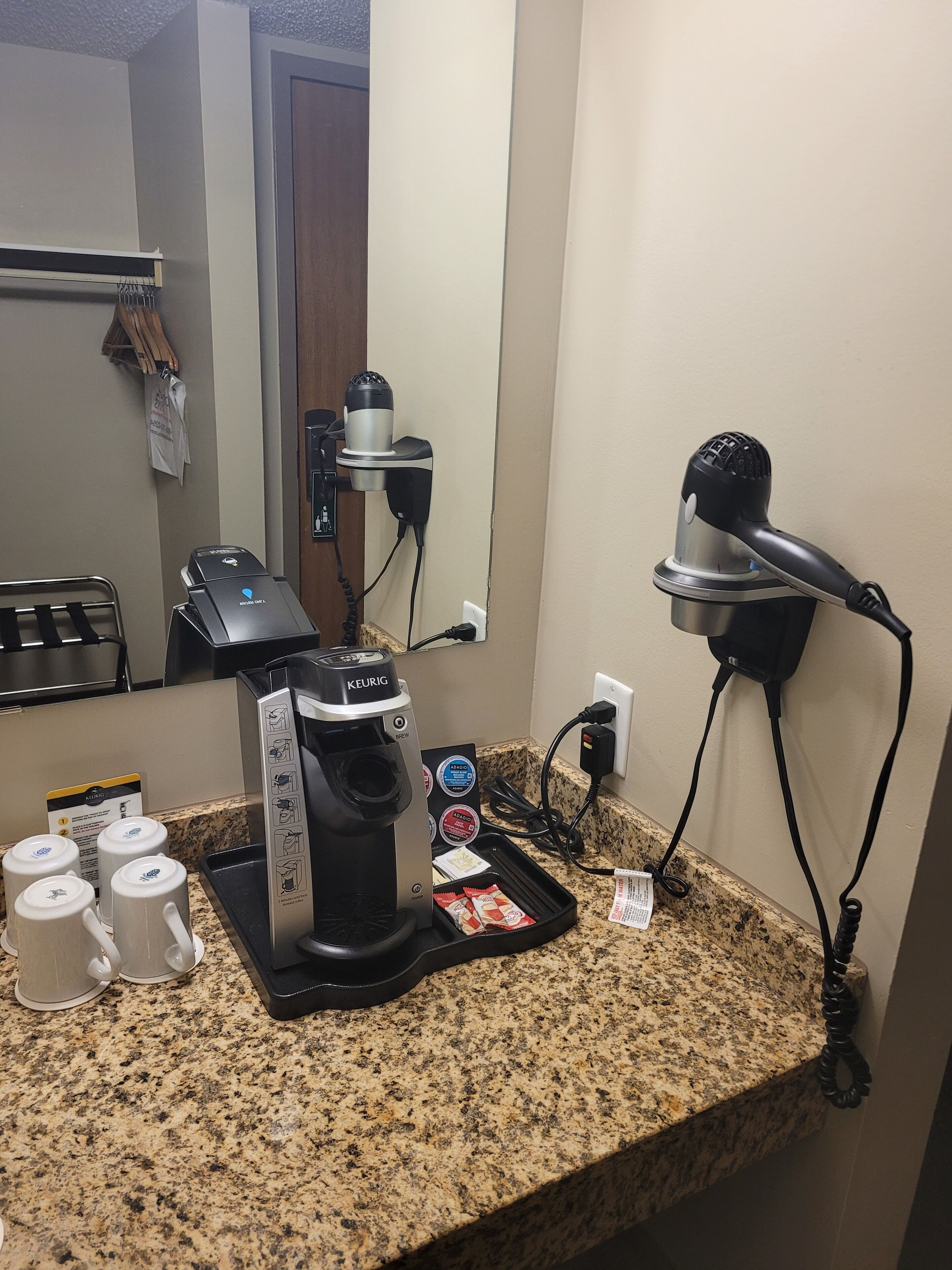 Une petite cuisine équipée d’une machine à café Keurig, d’un sèche-cheveux et d’une autre machine à café.