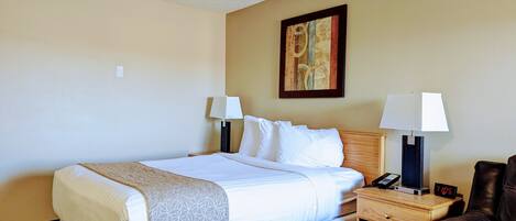 A hotel room with a bed, two bedside lamps, a clock, a leather chair, and a painting on the wall.