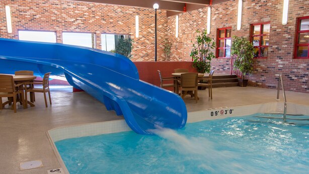 Una piscina con un tobogán azul y una pared de ladrillo al fondo.