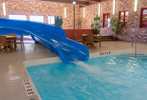 Una piscina con un tobogán azul y una pared de ladrillo al fondo.
