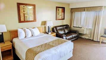 Quarto de hotel com uma cama grande, um sofá de couro, uma escrivaninha com abajur e um aparelho de ar condicionado.