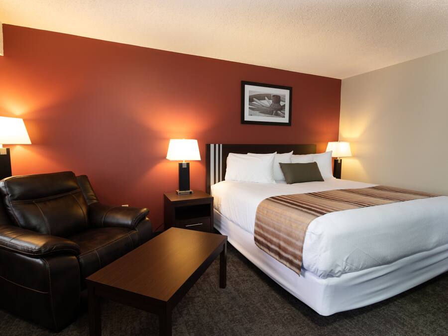 A hotel room with a bed, two bedside lamps, a nightstand, a leather armchair, and a wooden table.