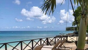 A wooden deck with lounge chairs facing a beach. - Tropical Sunset Beach Apartment Hotel (Holetown)