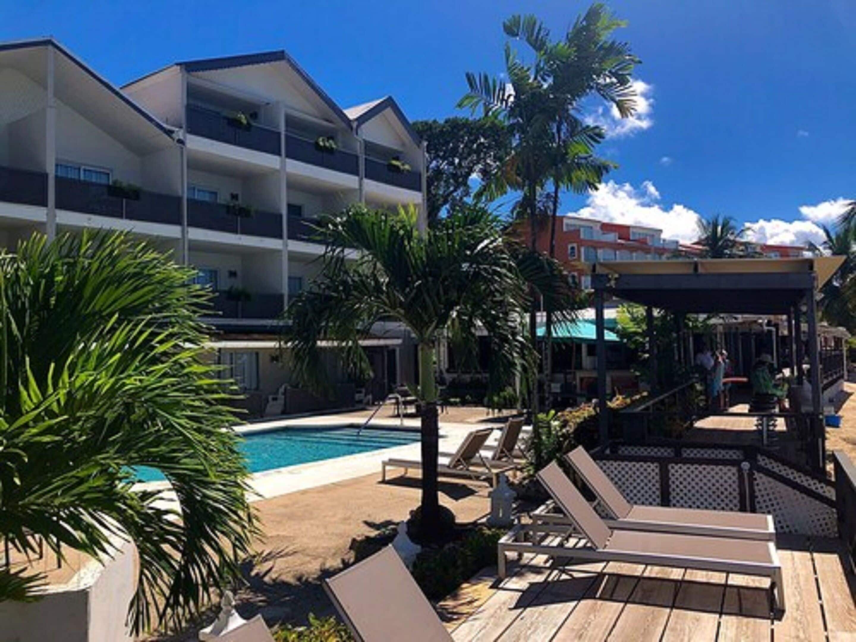 A hotel with a pool, lounge chairs, and a covered area with umbrellas.