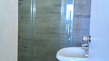 Ett badrum med en duschkabin i glas, ett vitt handfat och ett kaklat golv.