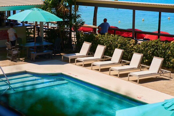 A pool area with lounge chairs, a table, and a view of the ocean.