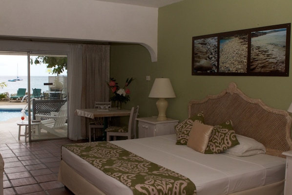 A hotel room with a bed, a table, chairs, a lamp, and a view of the sea. - Tropical Sunset Beach Apartment Hotel (Holetown)