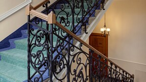 Una imponente escalera con barandales de metal negro ornamentados y un pasamanos de madera, que conduce a un piso superior.
