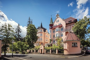 Un bâtiment historique doté de plusieurs tours et d’une tourelle, entouré d’arbres et surplombant un ciel dégagé.