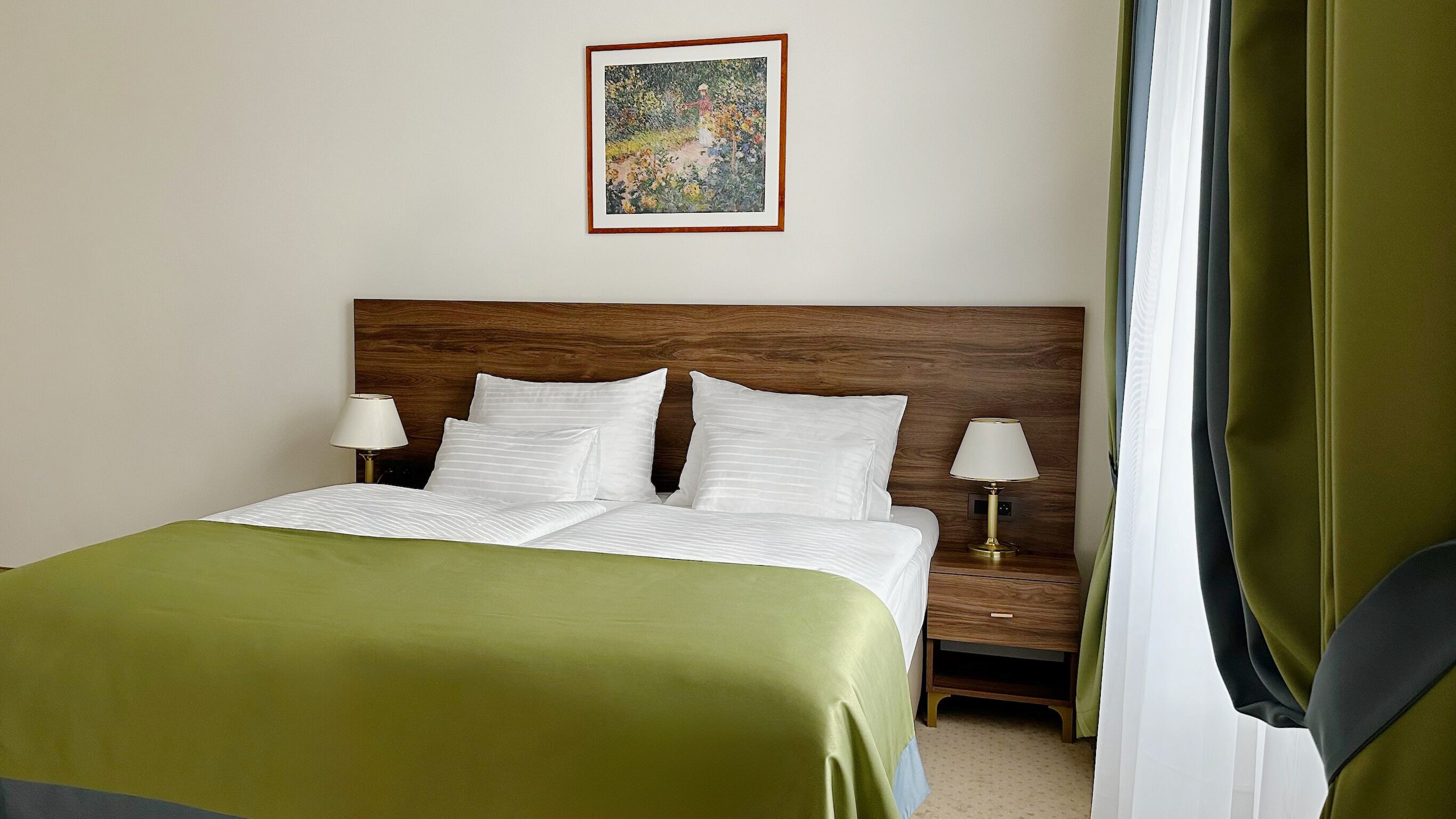 A neatly made bed with white linens, two bedside tables with lamps, a wooden headboard, and a framed painting on the wall.