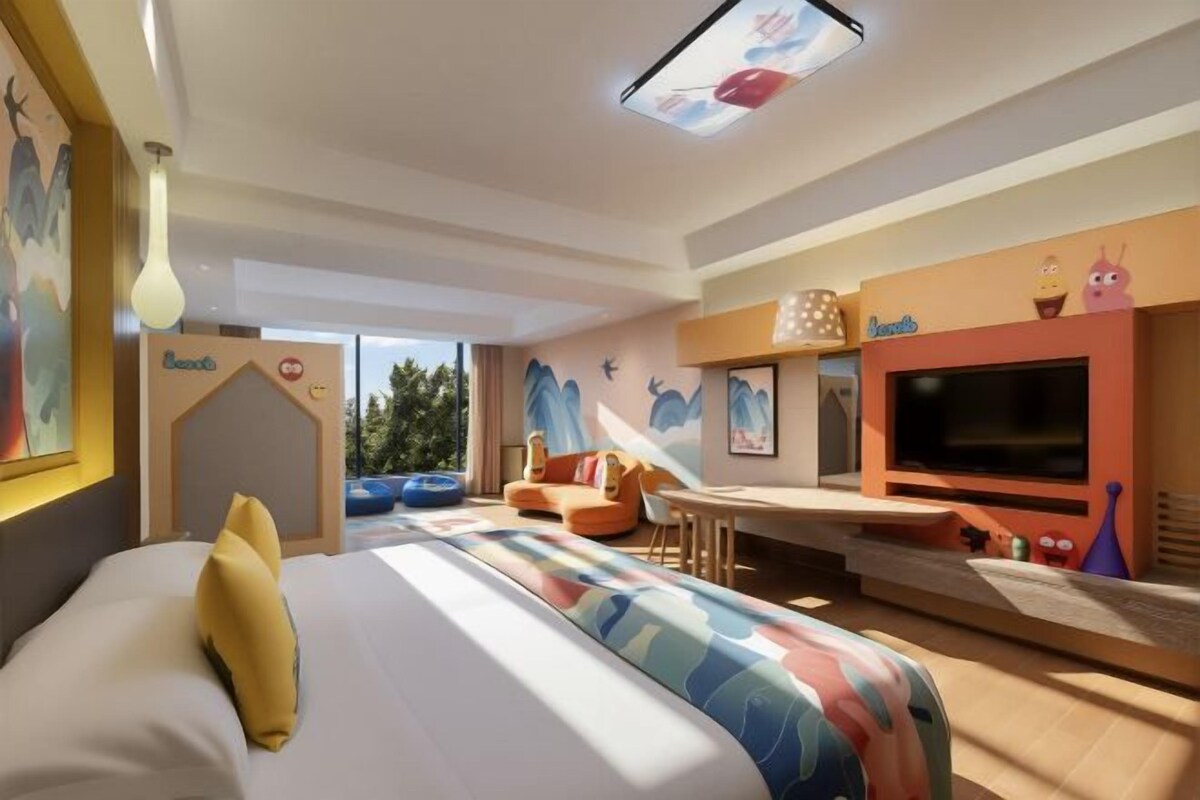 A modern hotel room with a large bed, a flat-screen TV, a dining area, and a view of the outdoors.