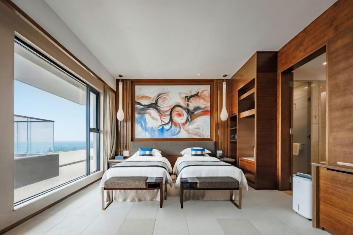 A modern bedroom with two beds, a large abstract painting, and a view of the city.
