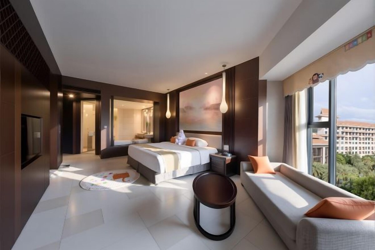 A modern hotel room with a large bed, a sofa, a round chair, and a view of the city.