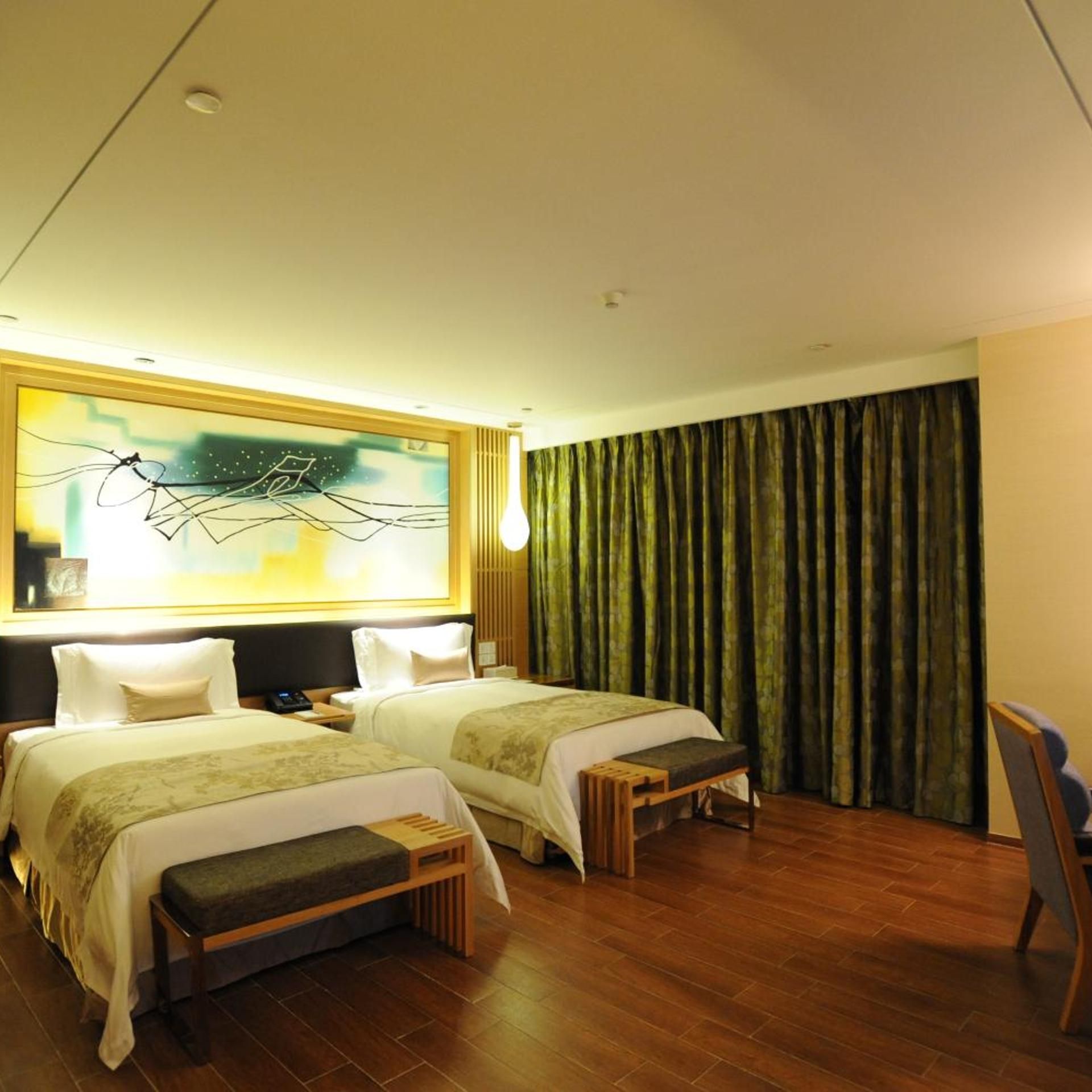 A hotel room with two beds, a large abstract painting on the wall, a wooden bench, and a view of the outside through sheer curtains.