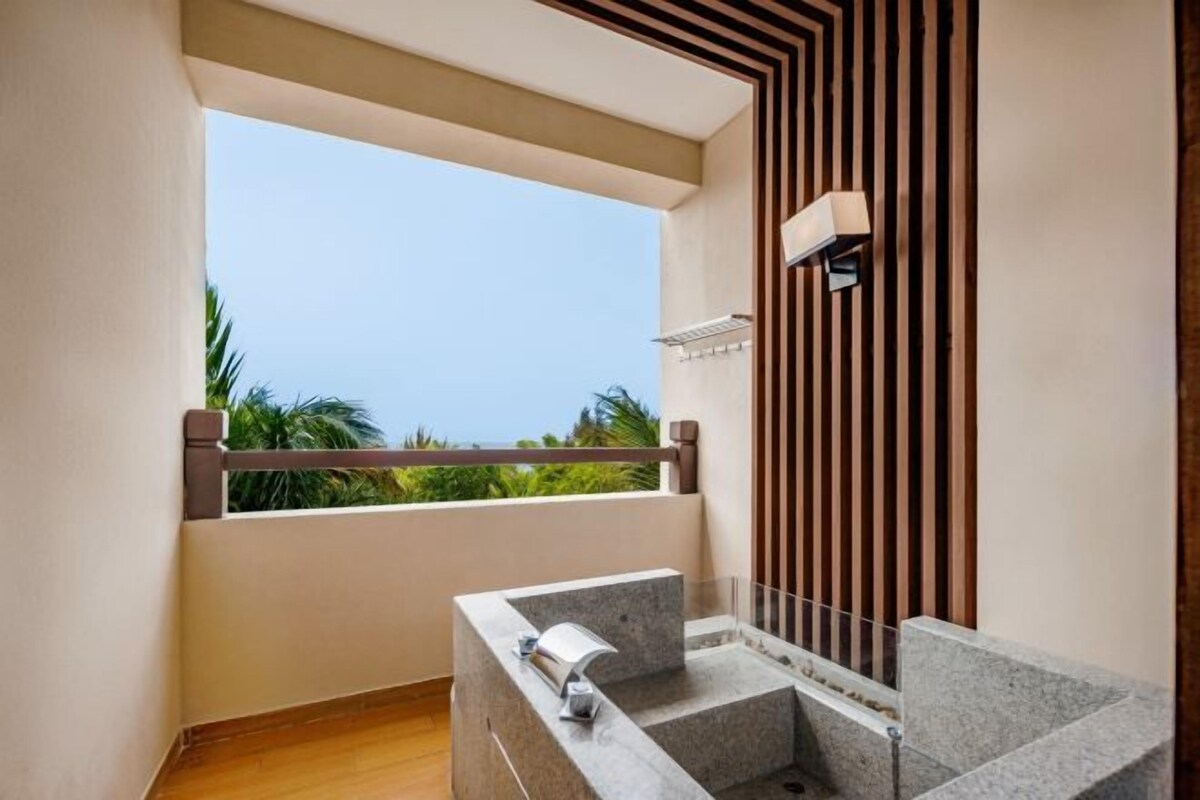 A modern bathroom with a freestanding bathtub, a window with a view of palm trees, and a wooden slat wall design.