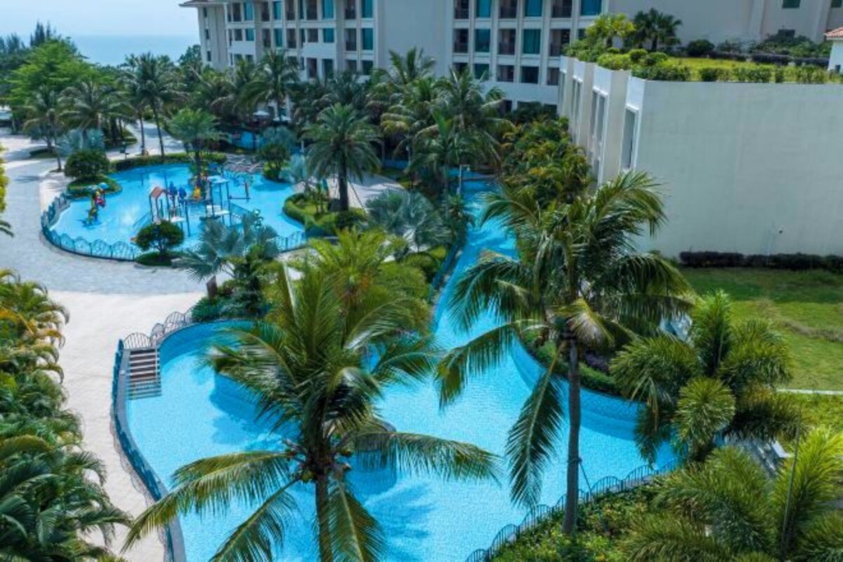 A resort with multiple swimming pools surrounded by palm trees and a large building in the background.