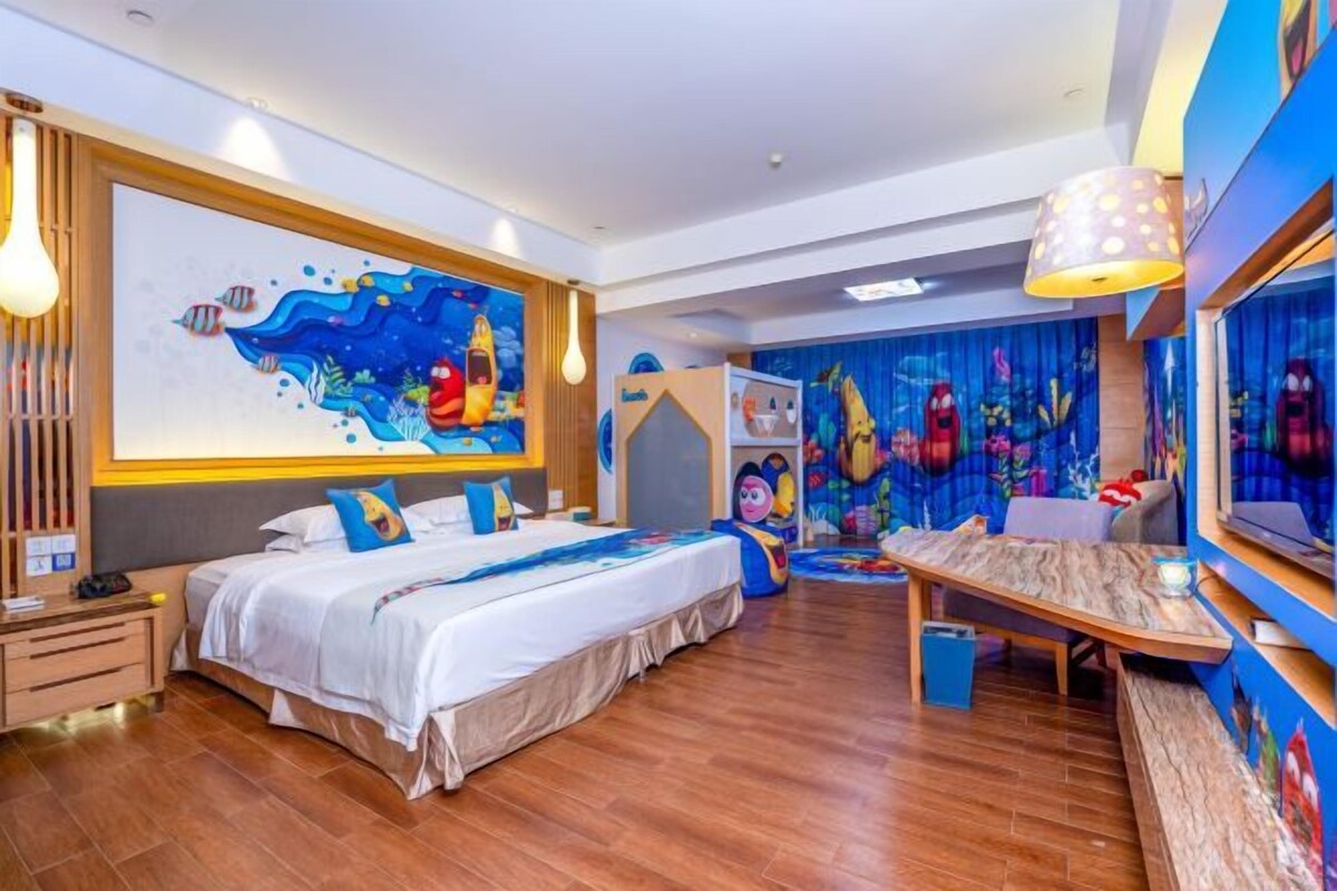 A hotel room with a large bed, a desk, and a mural of an underwater scene.