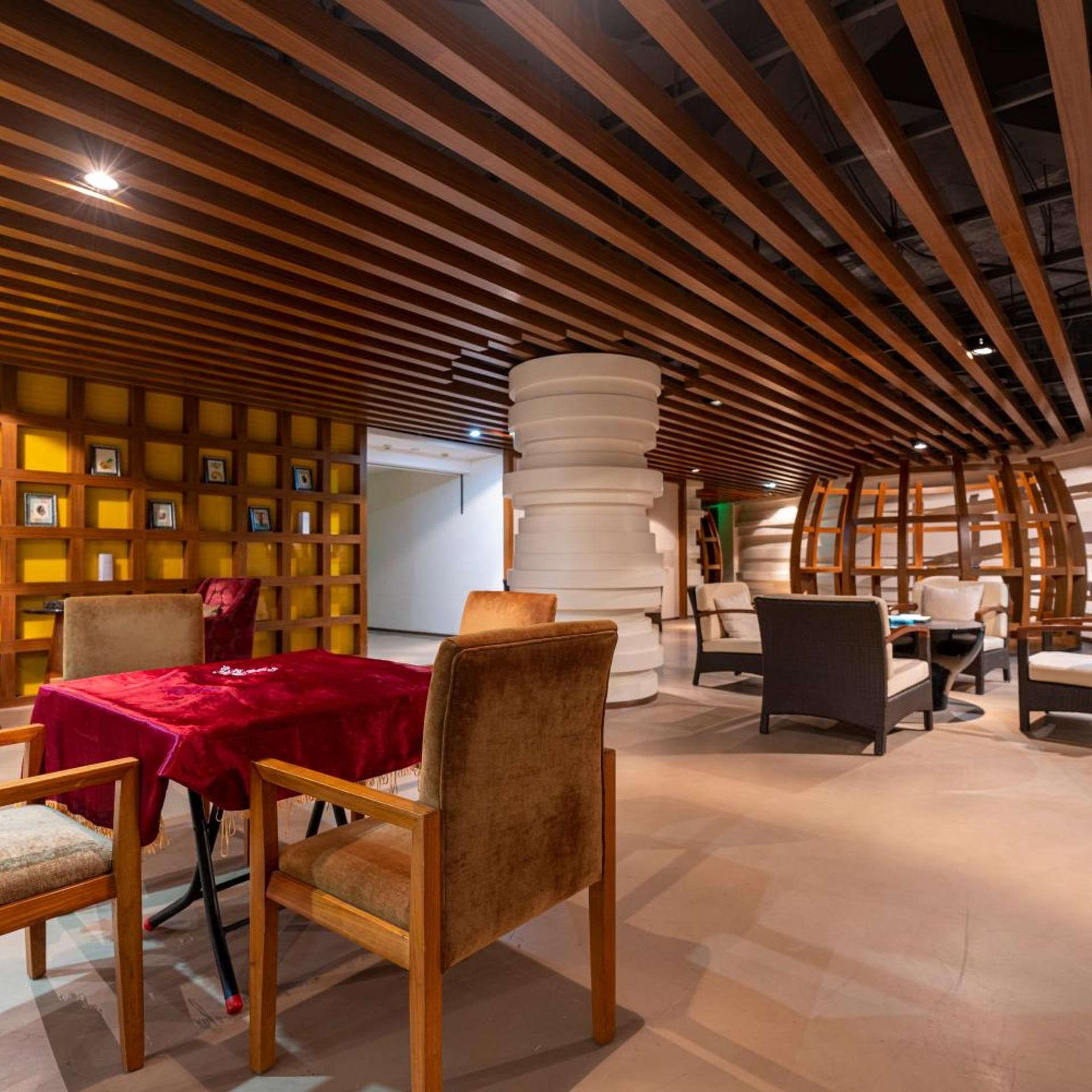 An interior space with a wooden slatted ceiling, a central white column, and seating arrangements.