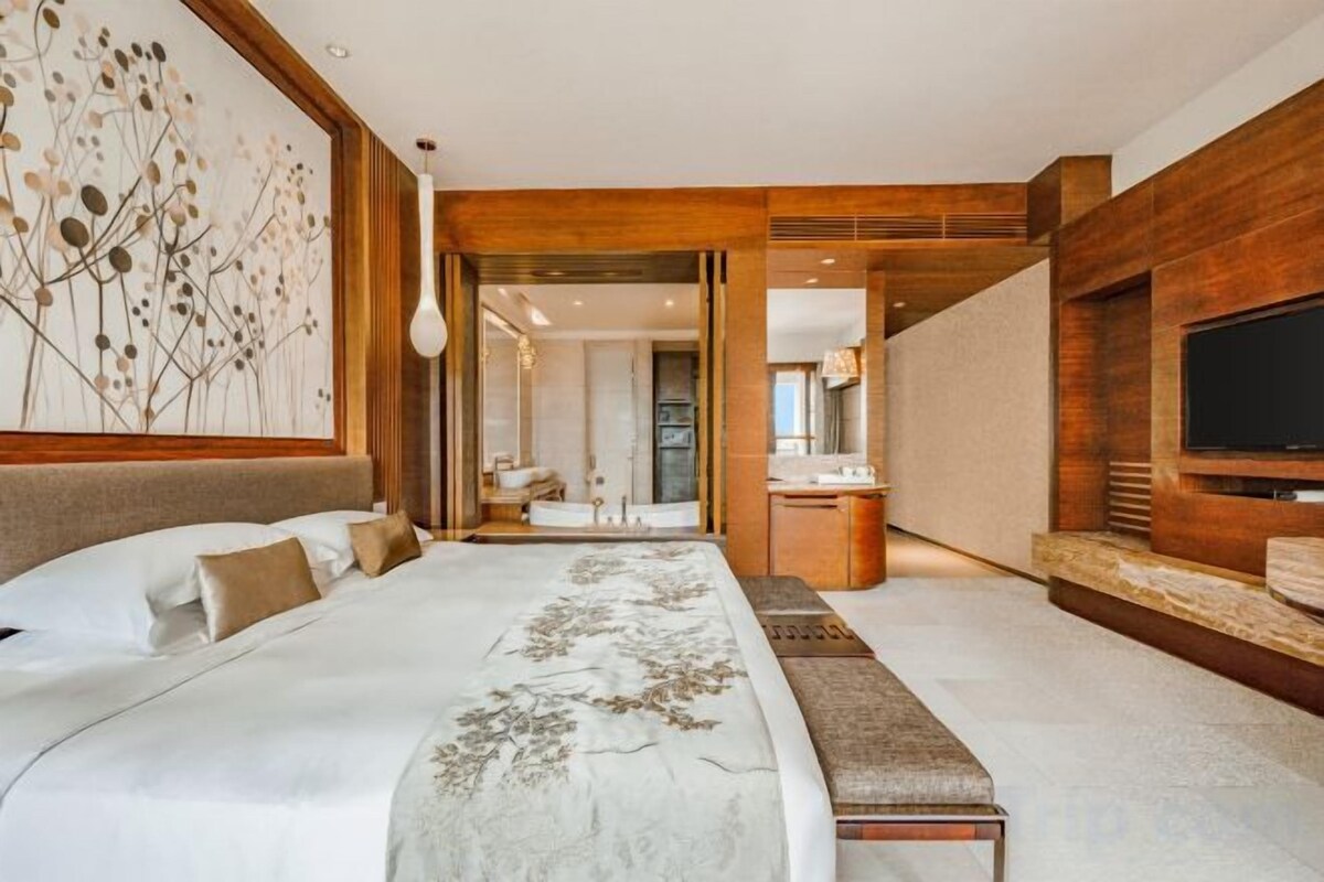 Una camera d'albergo moderna con un letto grande, una televisione e un bagno visibile attraverso una porta aperta.