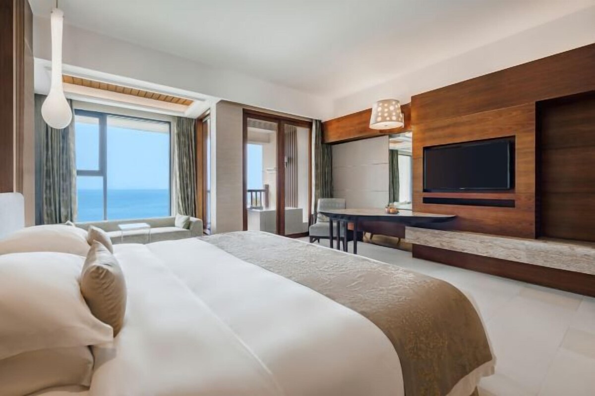A modern hotel room with a large bed, a desk, and a TV mounted on the wall.