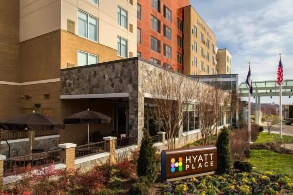 Exterior de hotel com uma placa indicando 'Hyatt Place', área de estar externa e uma bandeira.