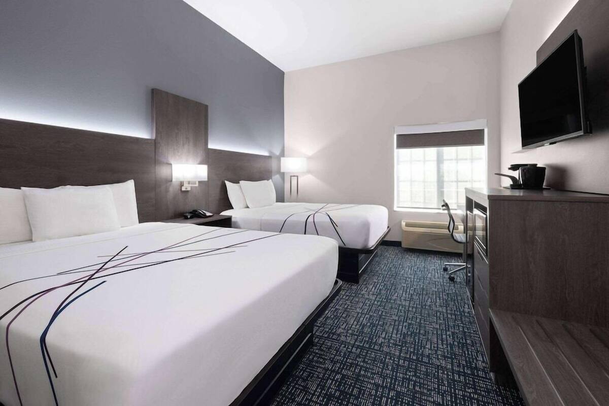 Une chambre d’hôtel avec deux lits, un bureau, un téléviseur à écran plat, une fenêtre et une kitchenette.