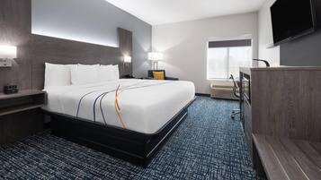 Ein Hotelzimmer mit einem großen Bett, Nachttischen, einem Schreibtisch, einem Sessel und einem Fernseher sowie einem Fenster.