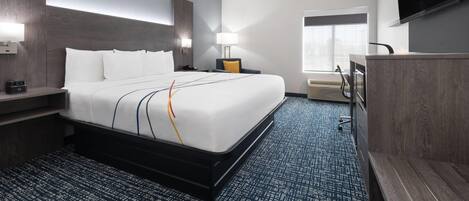 A hotel room with a large bed, bedside tables, a desk, a chair, a TV, and a window.