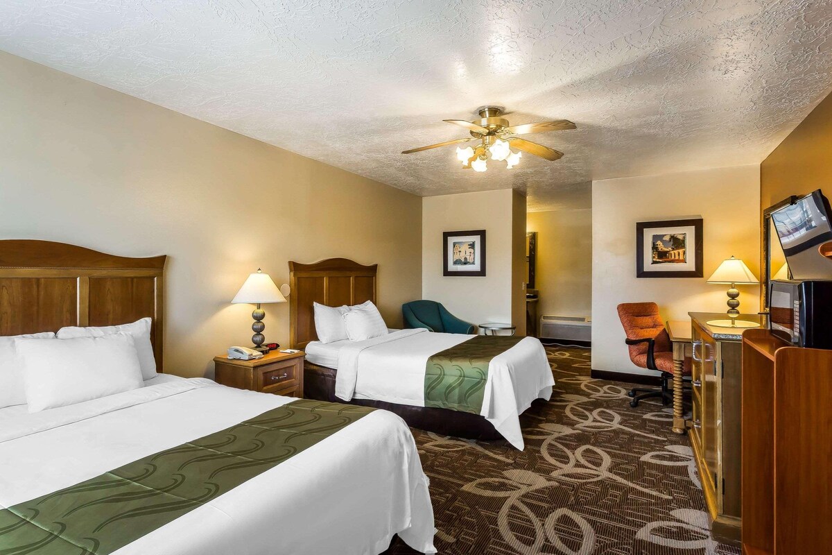 A hotel room with two beds, a desk, a chair, a television, and a ceiling fan.