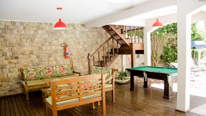 Une terrasse en bois avec une table de billard, un canapé agrémenté de coussins à motifs floraux et un escalier menant à un niveau supérieur.