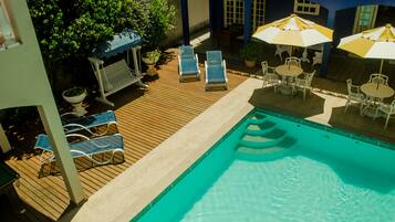 A pool area with lounge chairs and umbrellas, surrounded by a wooden deck and potted plants.