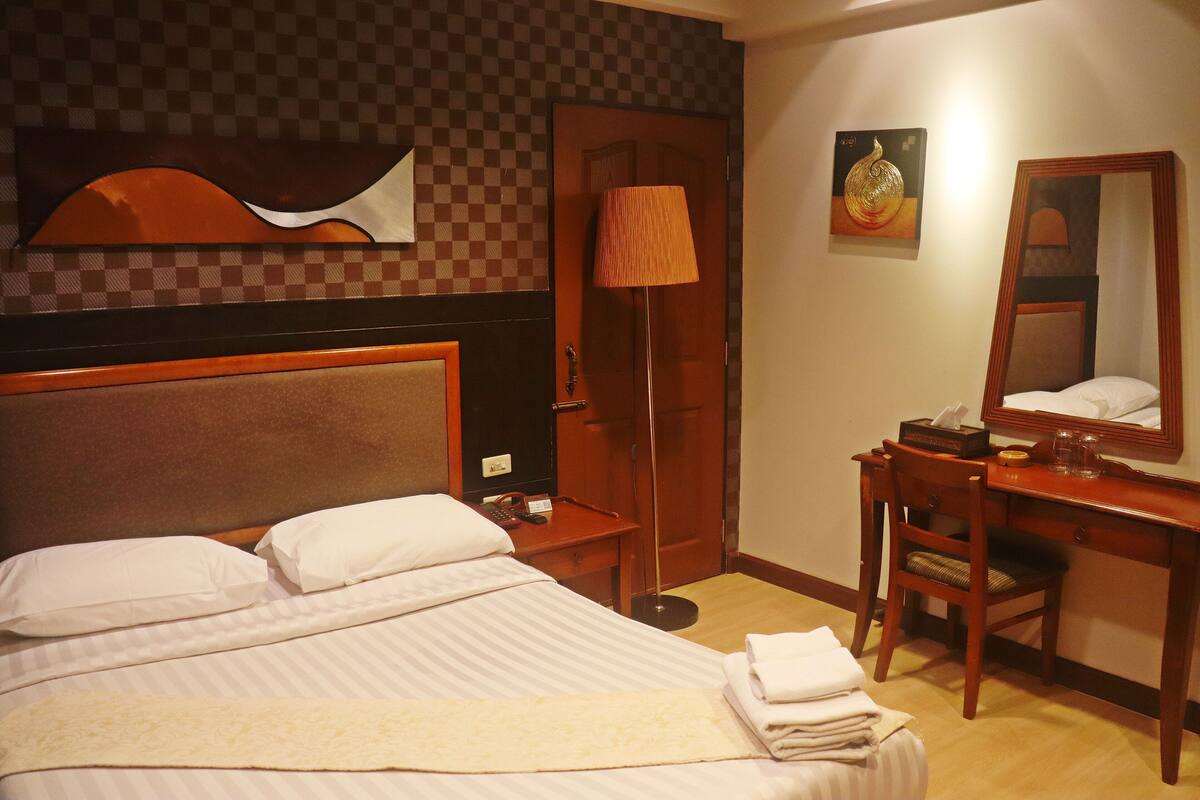 Hotellihuone, jossa on sänky, työpöytä, tuoli, lamppu, peili ja ovi.