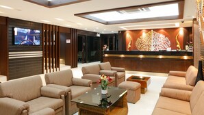 A hotel lobby with a reception desk, sofas, a coffee table, and a TV screen. - Inn House Hotel (Pattaya)