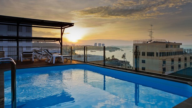 A swimming pool with lounge chairs and a view of the sunset over the water. - Inn House Hotel (Pattaya)