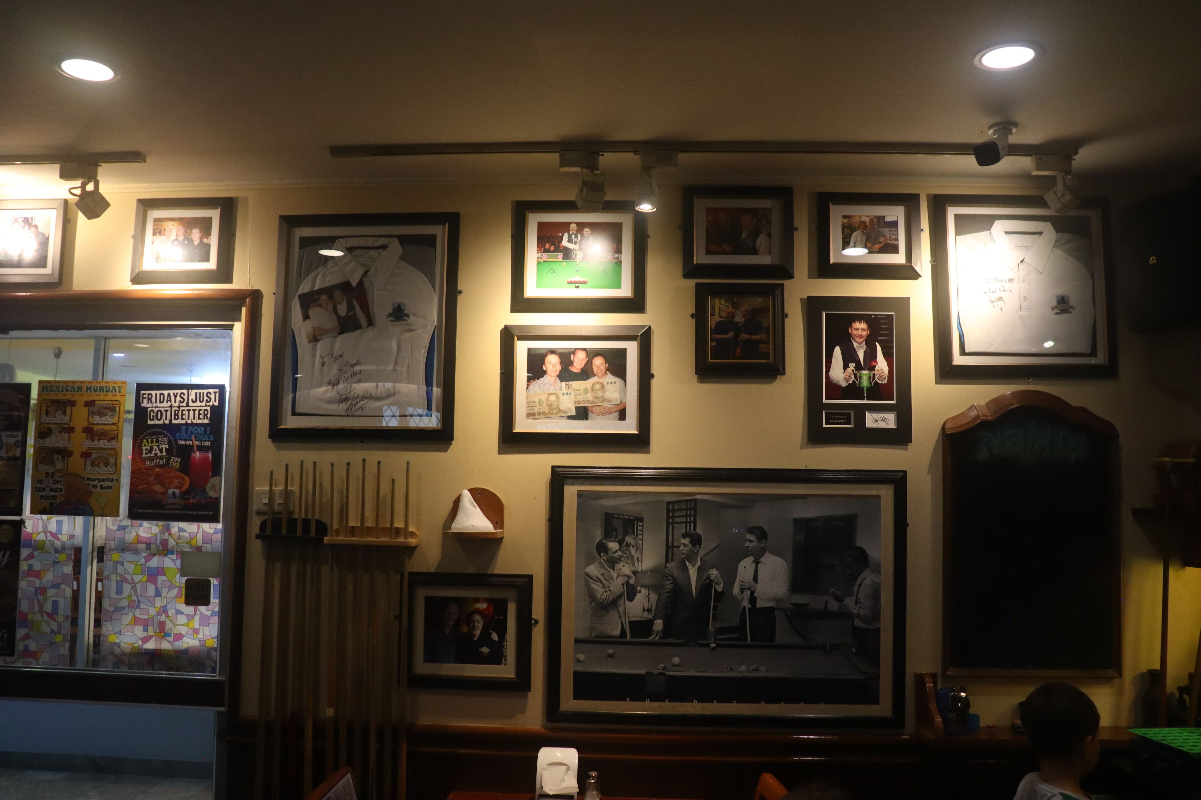 A room with a billiards table, framed photographs on the wall, and a window with a view of the outside.