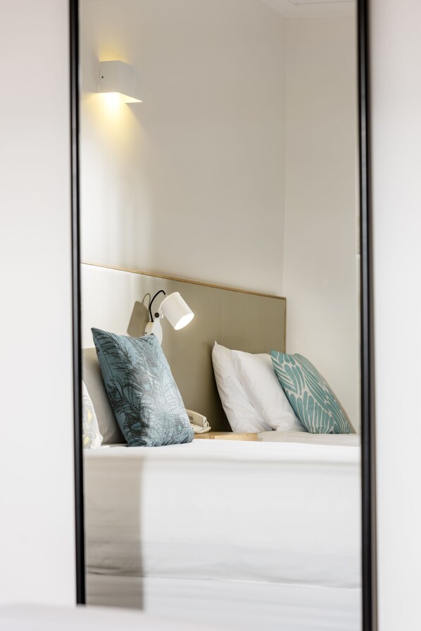 A hotel room with a bed, a nightstand, a lamp, and a mirror.