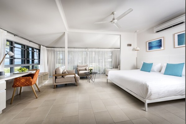 A modern hotel room with a large bed, a desk, a chair, a sofa, and a small table.