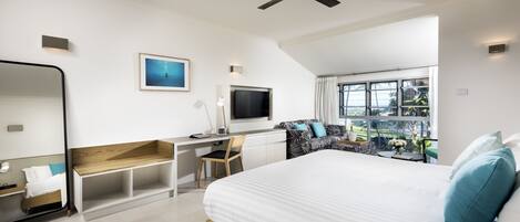 A modern bedroom with a large bed, a desk, a chair, a TV, and a view of the outdoors.