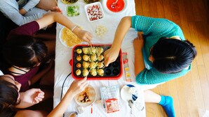 Un groupe de personnes est assis autour d’une table, devant de la nourriture et un plateau rouge rempli de différents plats.