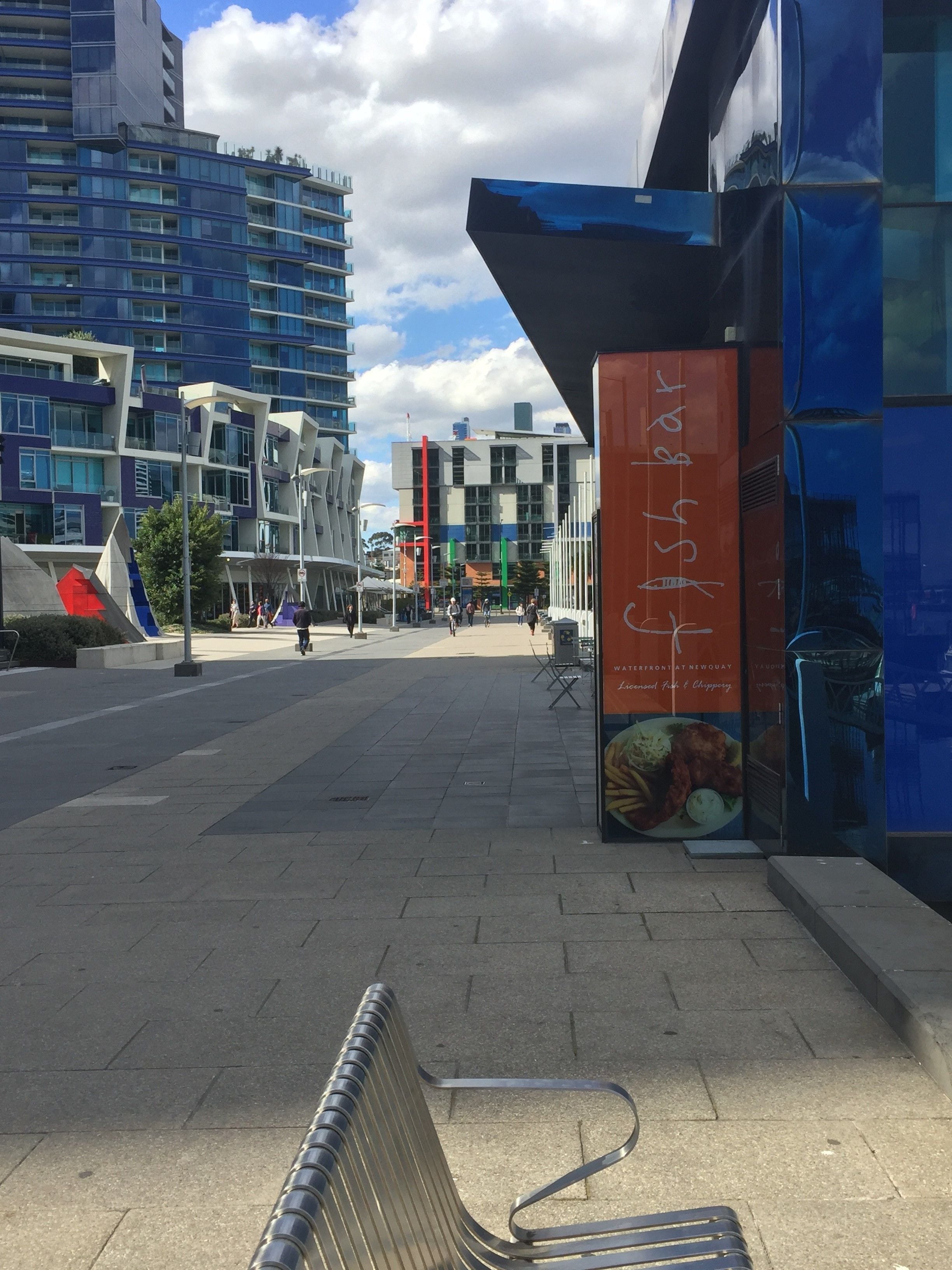 A modern urban street with a bench, a food advertisement, and contemporary buildings.