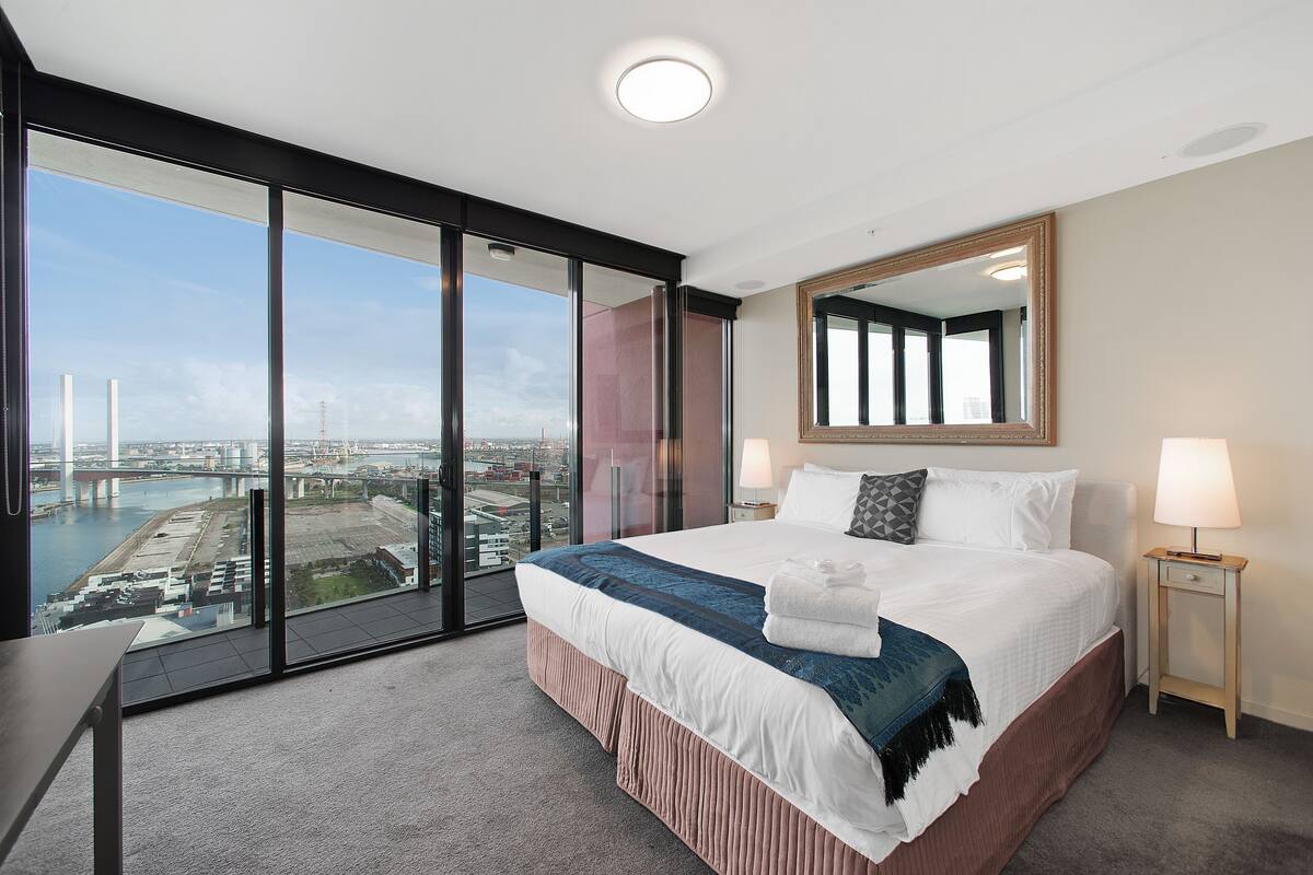 A hotel room with a large bed, a nightstand, a mirror, and a view of a bridge and river.