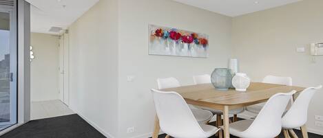 A modern dining area with a wooden table and white chairs, a large abstract painting on the wall, and a city view through a glass door.