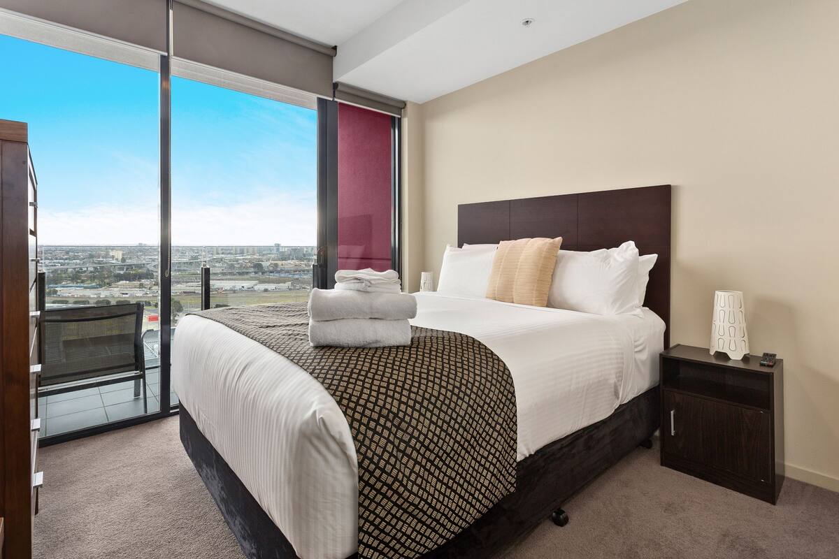 Une chambre d’hôtel avec un grand lit, une table de chevet, une chaise et une vue sur la ville.