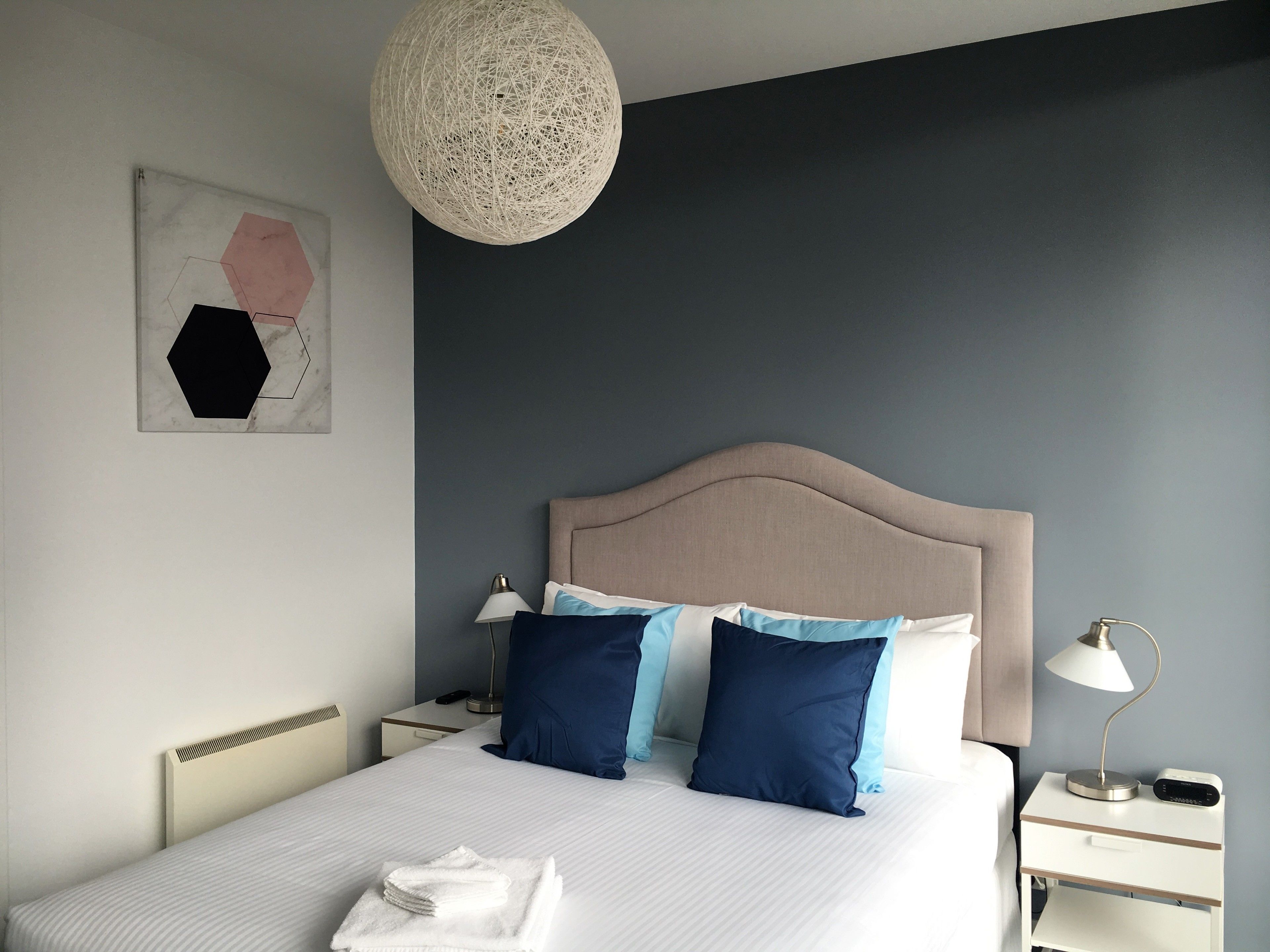A neatly made bed with a headboard, two bedside tables, a lamp, and a wall art piece.