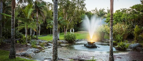 A serene garden with a central water feature, surrounded by lush greenery and palm trees.