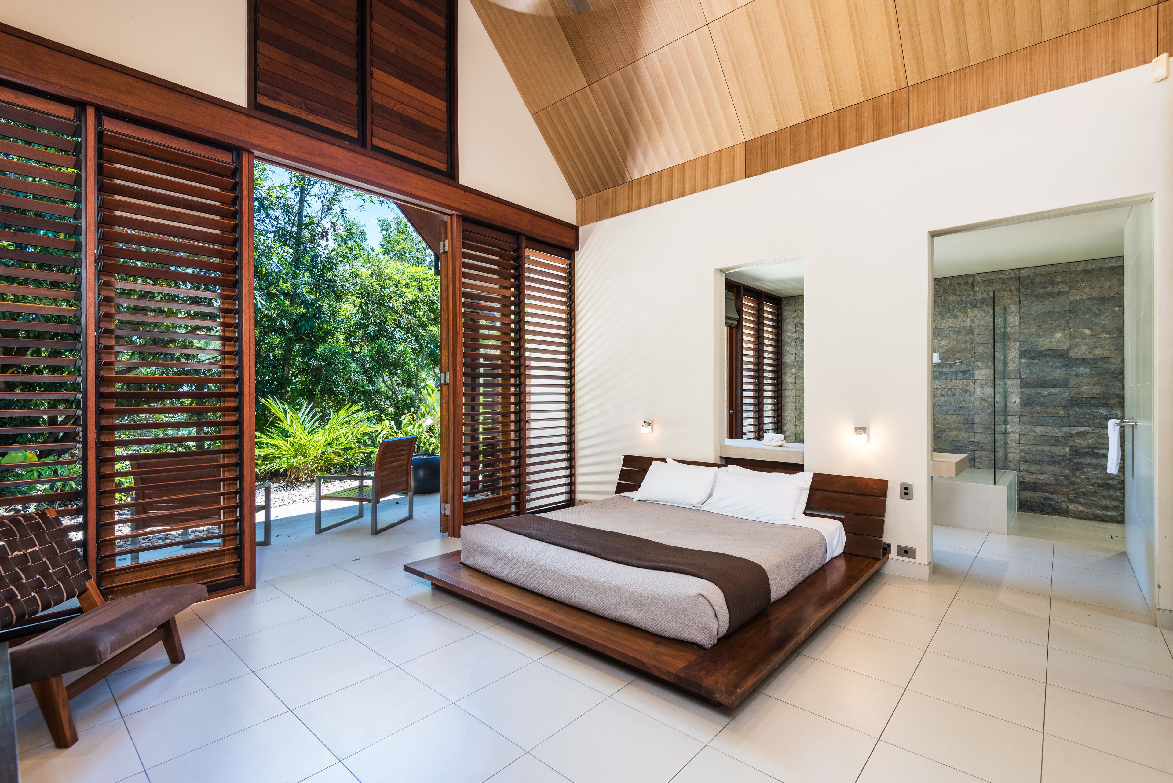 A modern bedroom with a large bed, wooden floor, and a view of greenery outside.